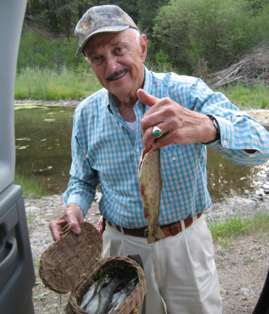 Harry A. Merlo holds up a fish near a stream, showing off his day's catch.