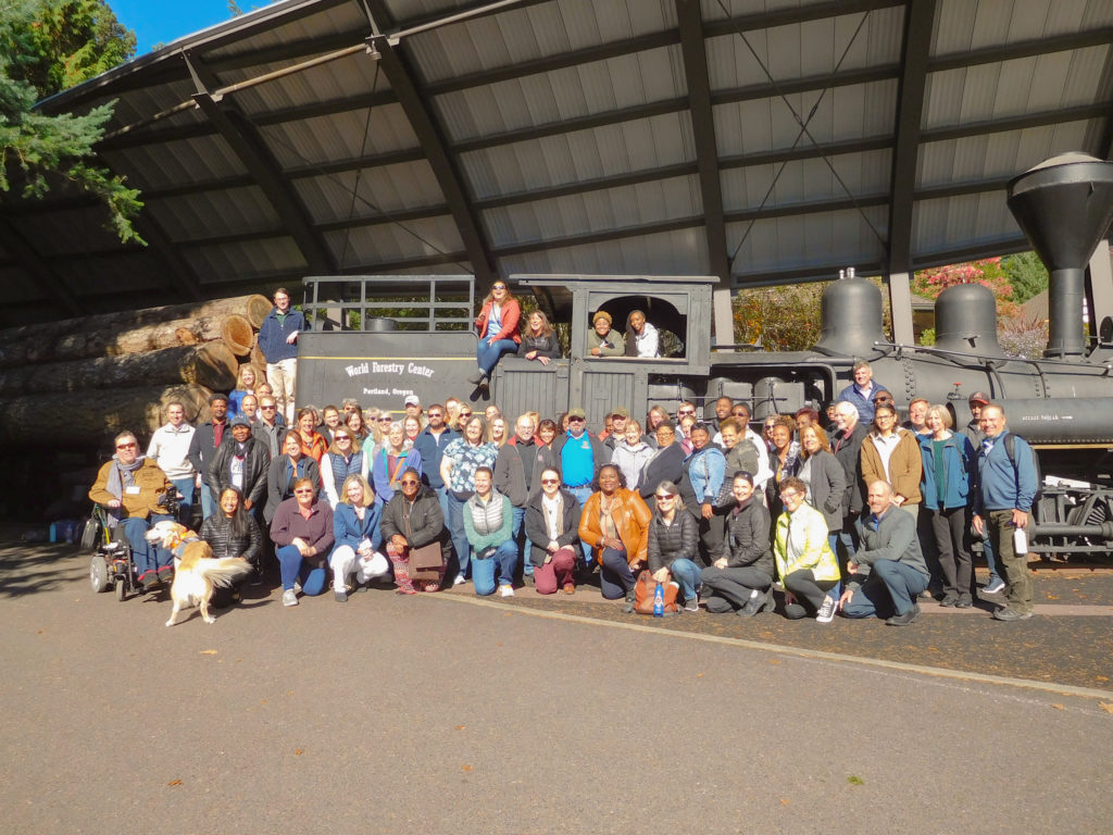 A group of guests gathers in front of an old train for a picture.