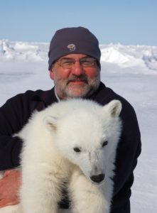 Man holding polar bear cub in the Arctic.